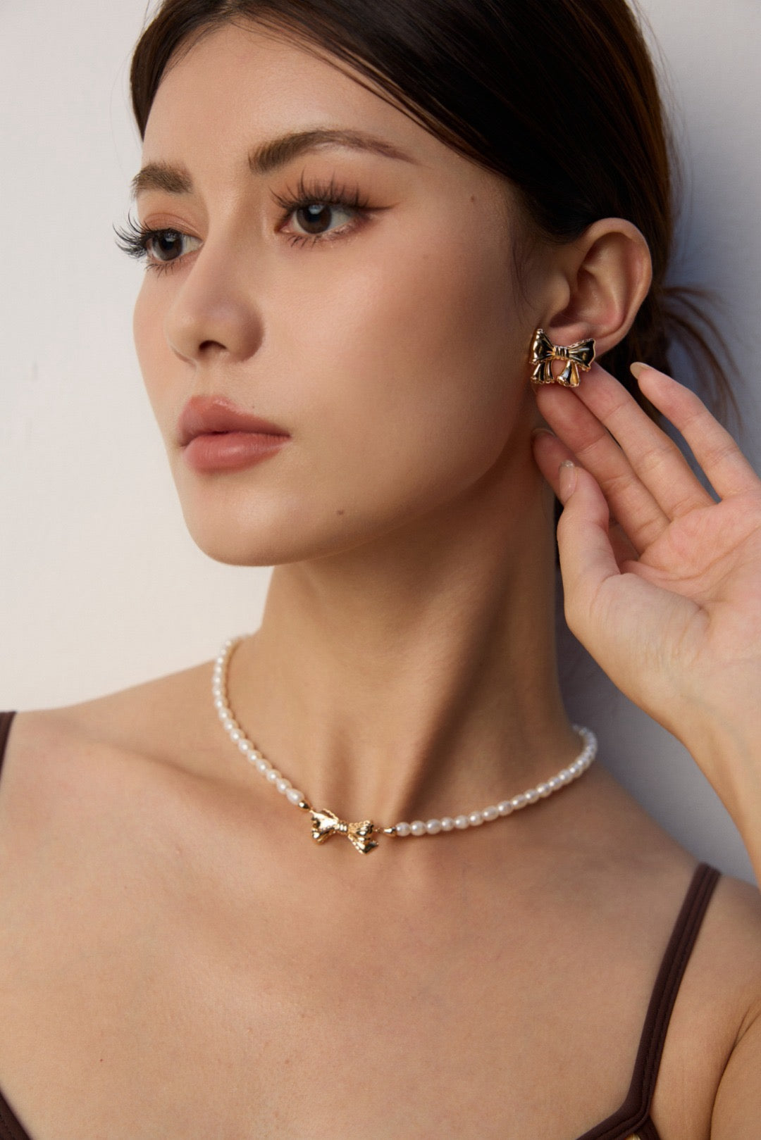 Woman wearing a pearl necklace and gold earrings against a neutral background
