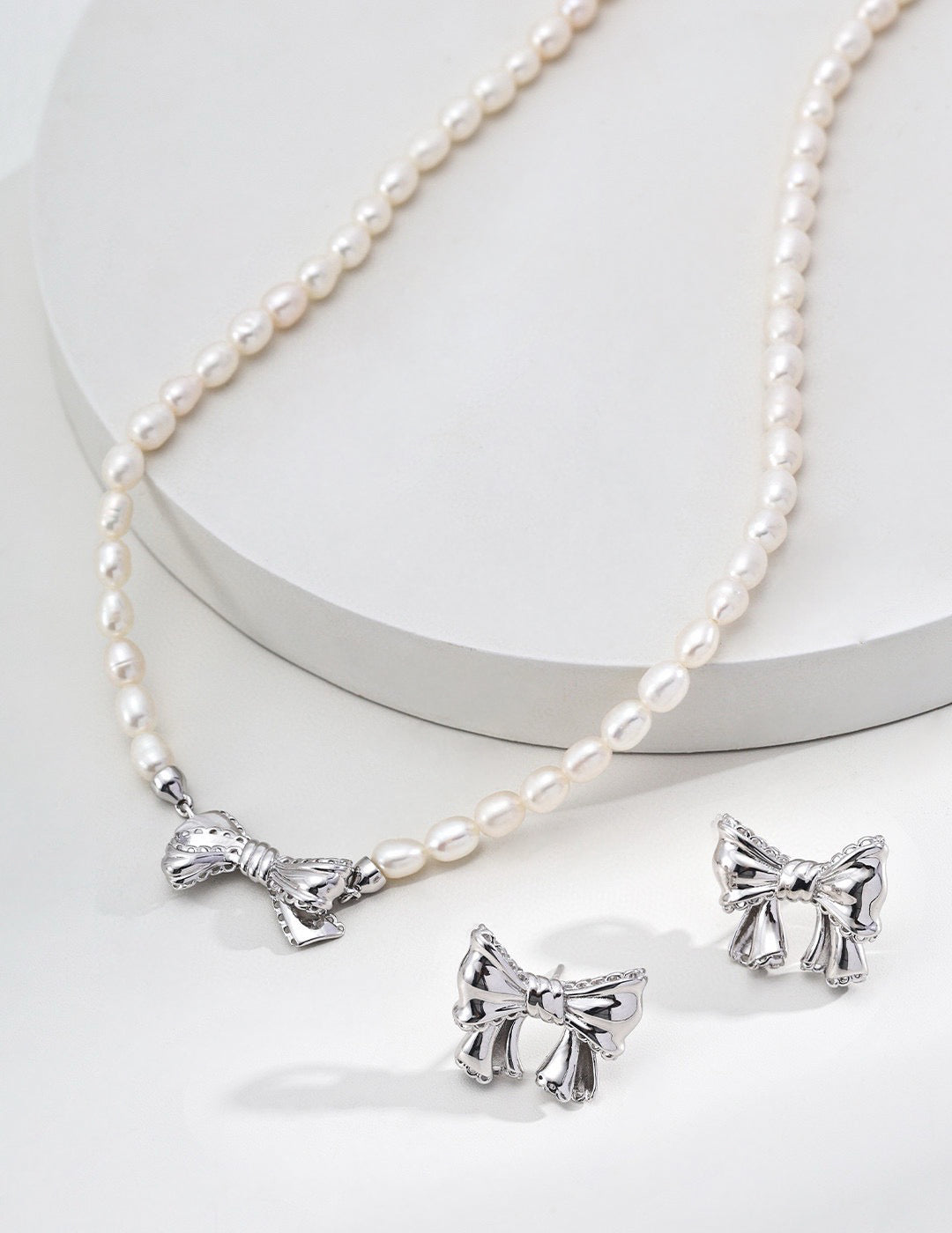 Pearl necklace with silver bow pendants on a white background
