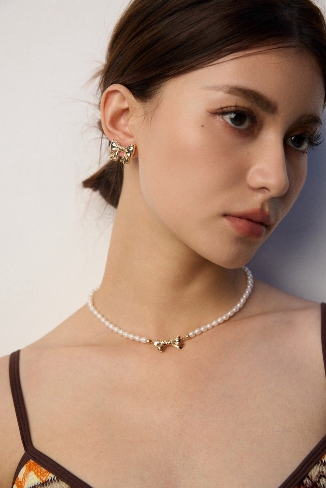 Woman wearing a pearl choker necklace with a gold pendant on a plain background