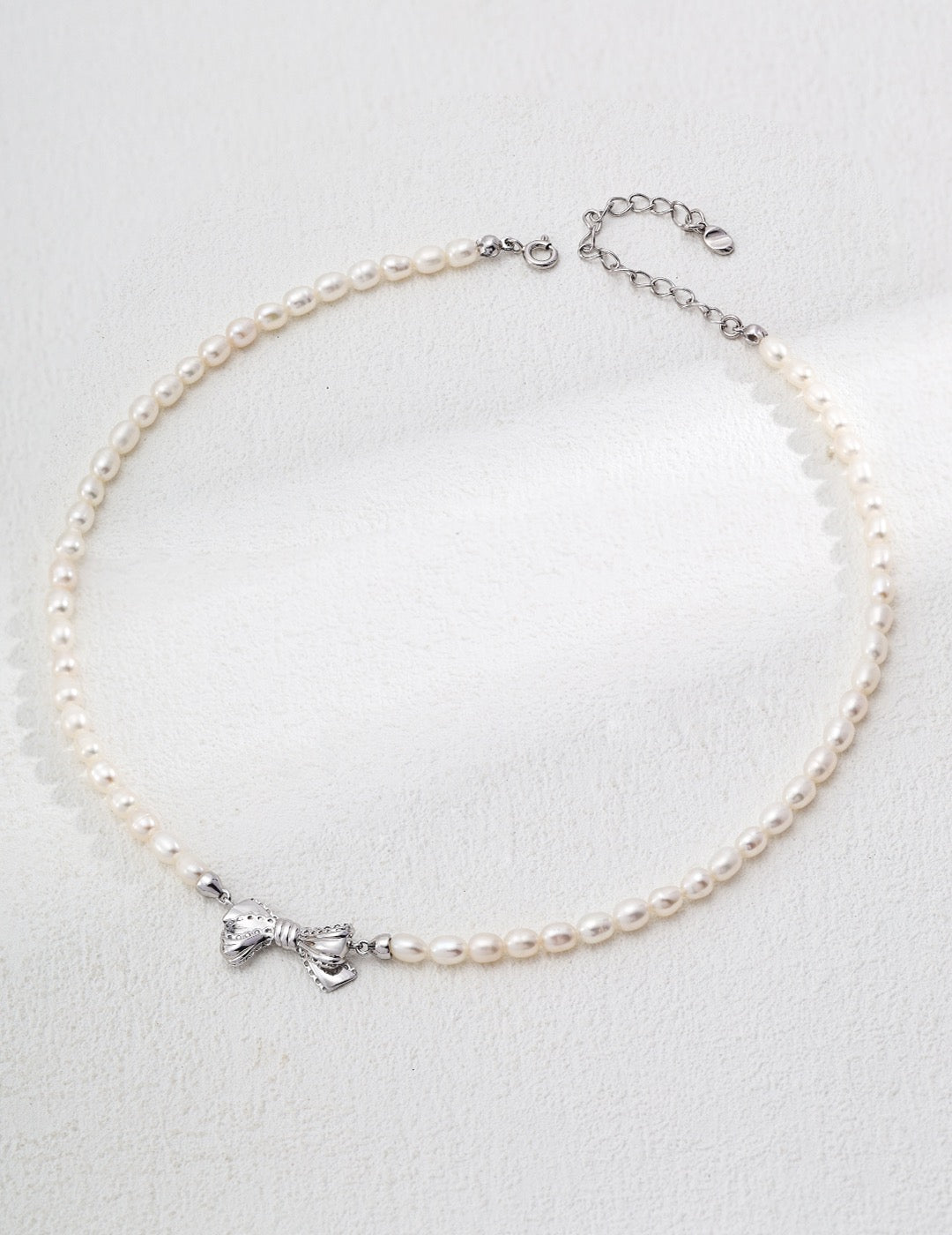 Pearl anklet with a silver bow charm on a light gray background