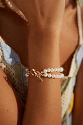 A person wearing a gold-colored bracelet with two chains of freshwater pearls on their wrist.