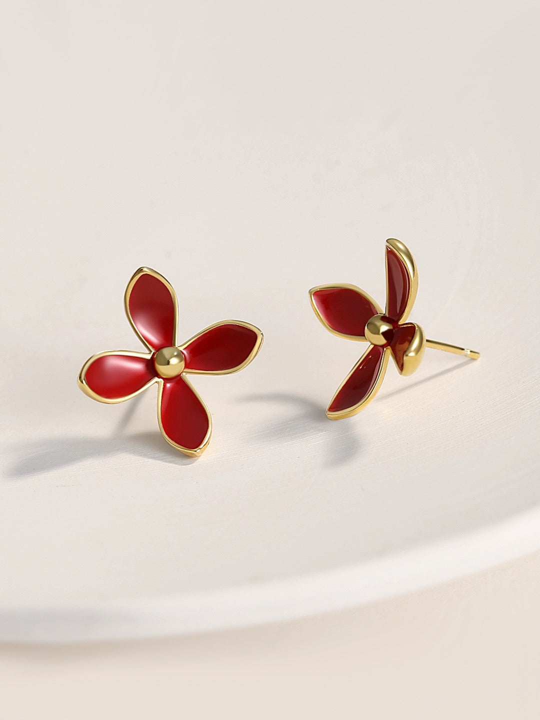 Red flower-shaped earrings with gold accents on a light beige background