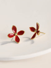 Red flower-shaped earrings with gold accents on a light beige background