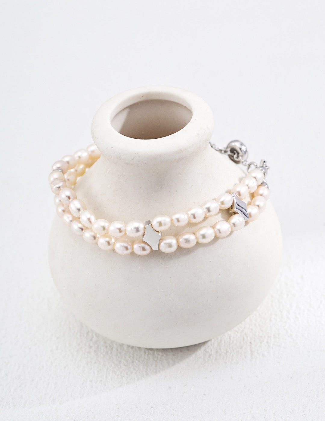 Pearl bracelet on a white ceramic vase with a white background