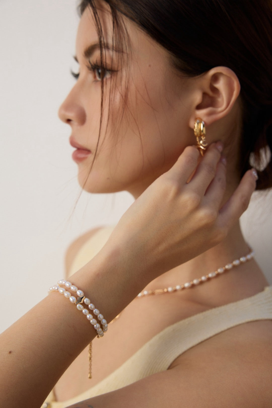 Woman wearing gold hoop earrings and pearl jewelry against a neutral background