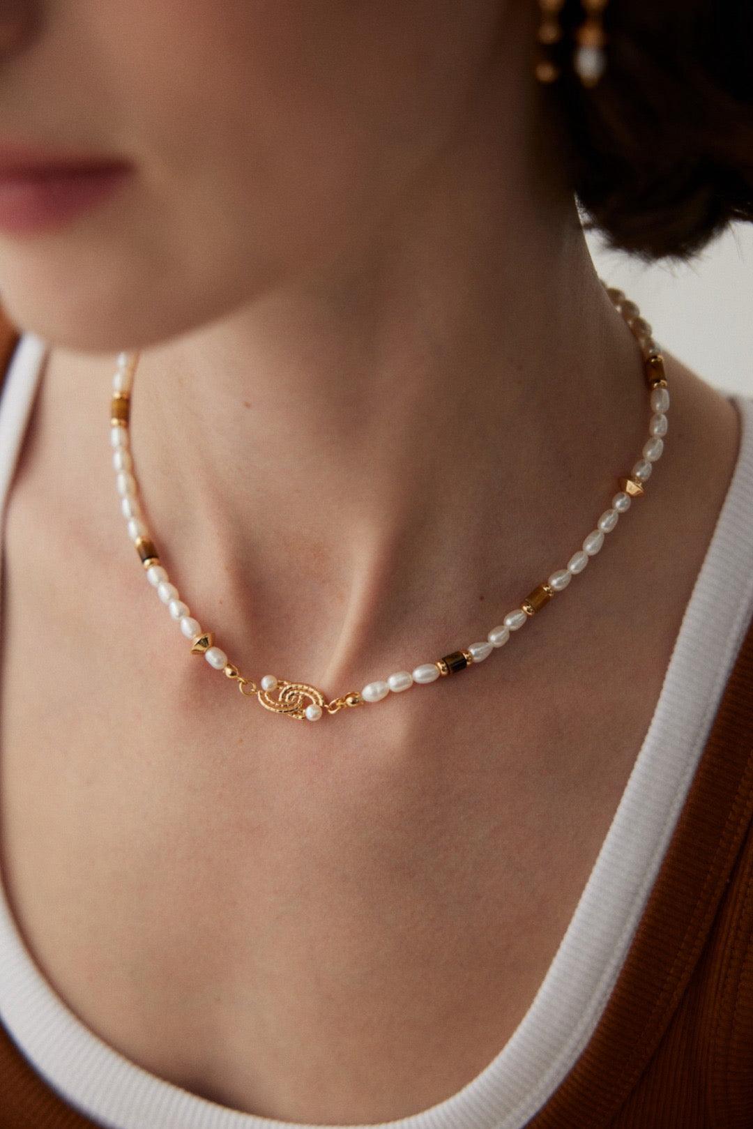 A close-up shot of the Tiger Eye Pearl and gold pendant accents necklace worn by a woman.
