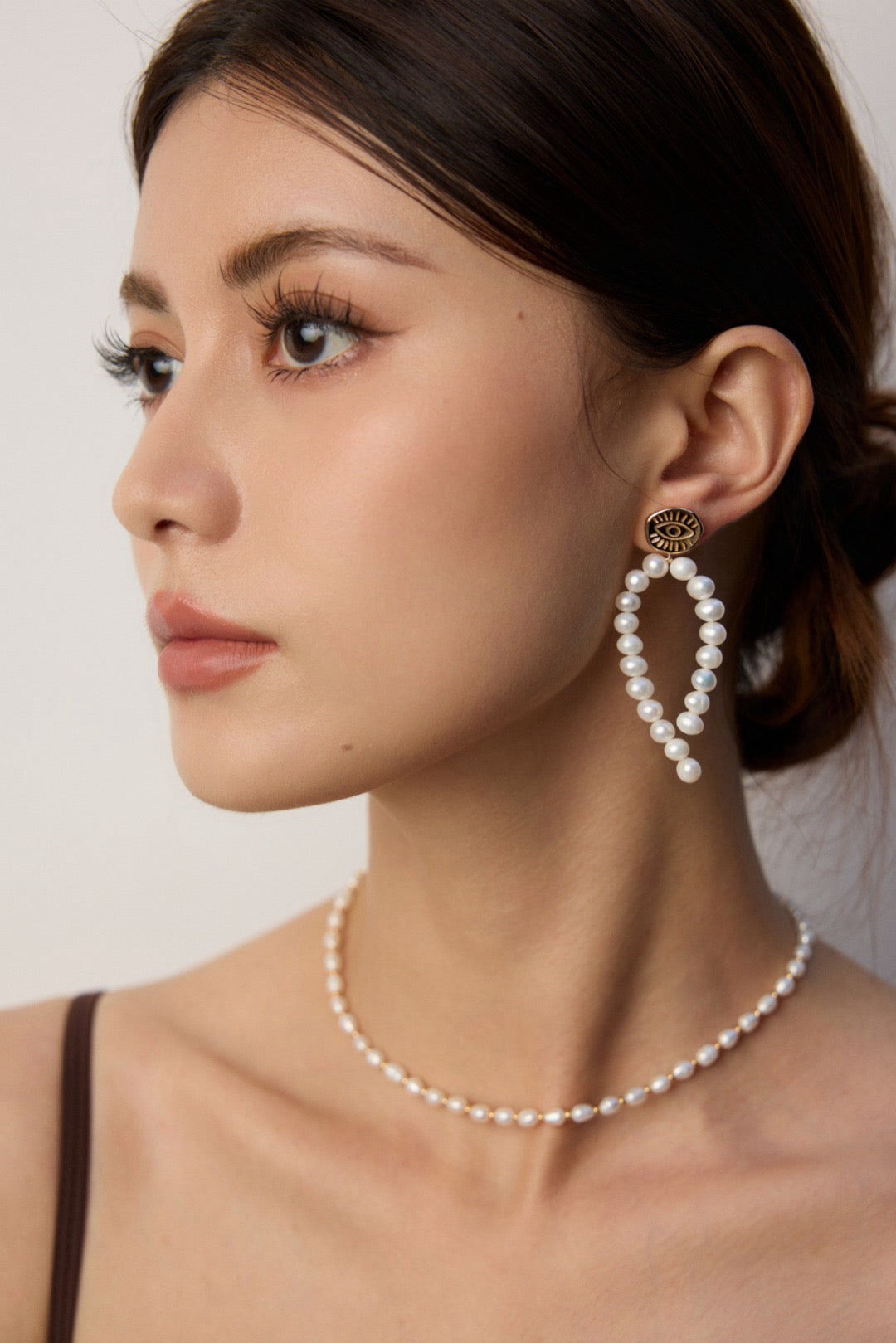 Woman wearing pearl earrings and necklace against a neutral background