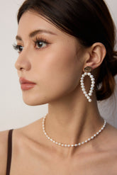 Woman wearing pearl earrings and necklace against a neutral background