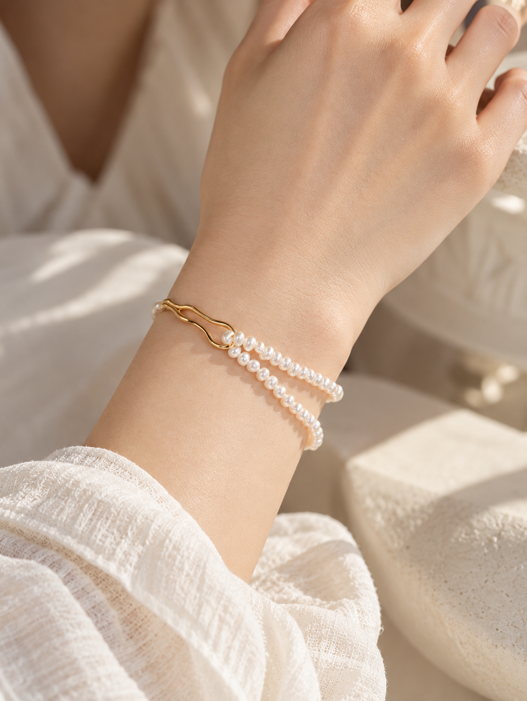 Duet Strand Pearl Slider Bracelet on a model's wrist, with two rows of freshwater pearls and an 18K gold vermeil wave bar