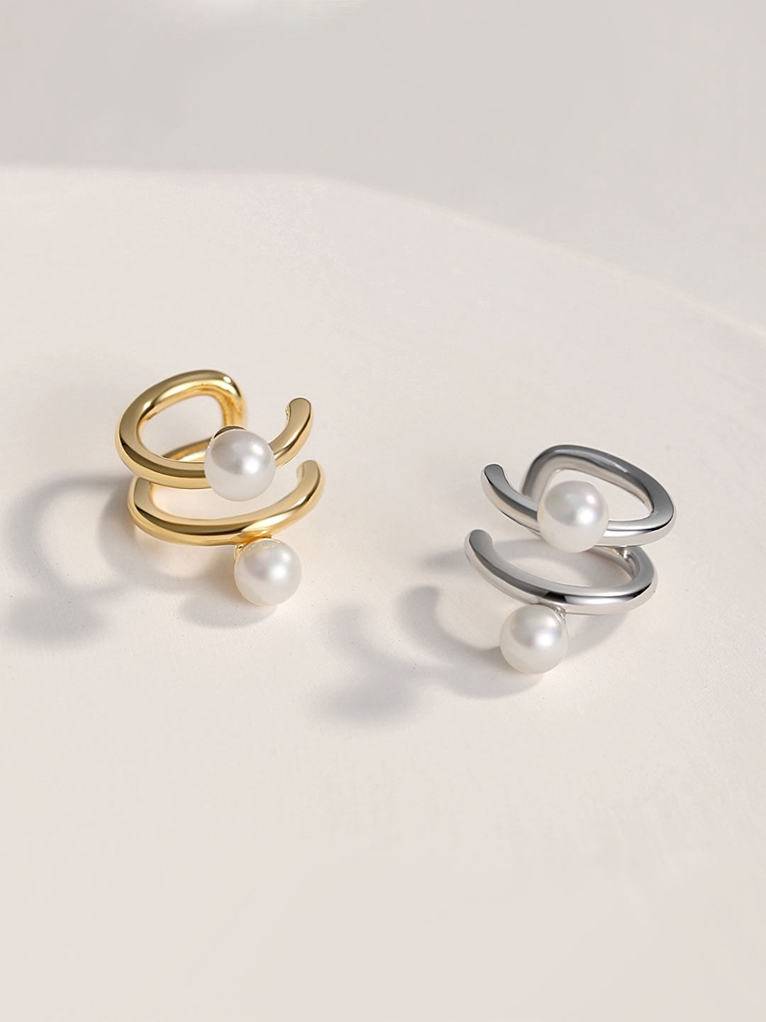 Two ear cuffs with 2 freshwater pearls inlay, gold and silver displayed on the white background.