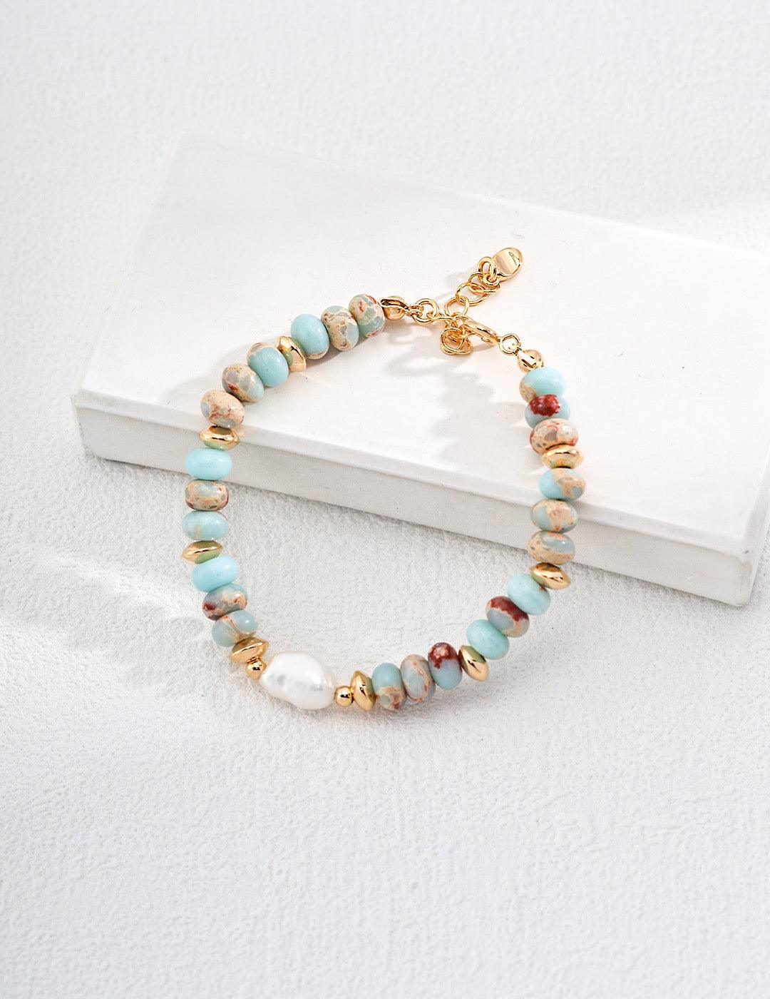 The Edith Bracelet showcases naturally beautiful figure stone beads in soft aqua and earthy tones, elegantly paired with lustrous baroque freshwater pearls and gleaming 18K gold vermeil displayed on the white rock.