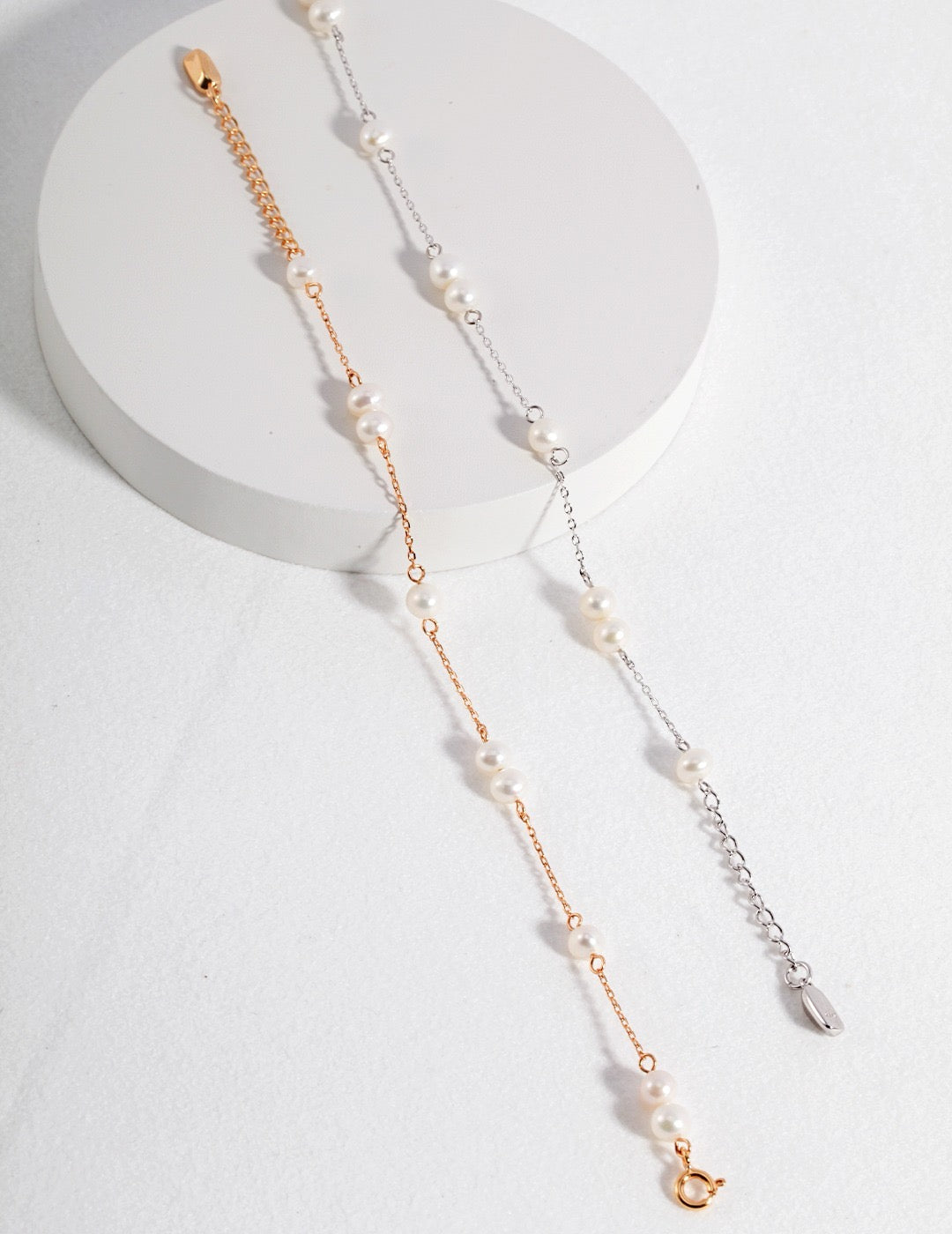 Gold and silver chain bracelets with freshwater pearls displayed on a white surface