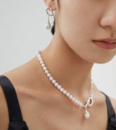 A close-up image of a person wearing an asymmetrical pearl necklace with a silver finish and irregular shapes.