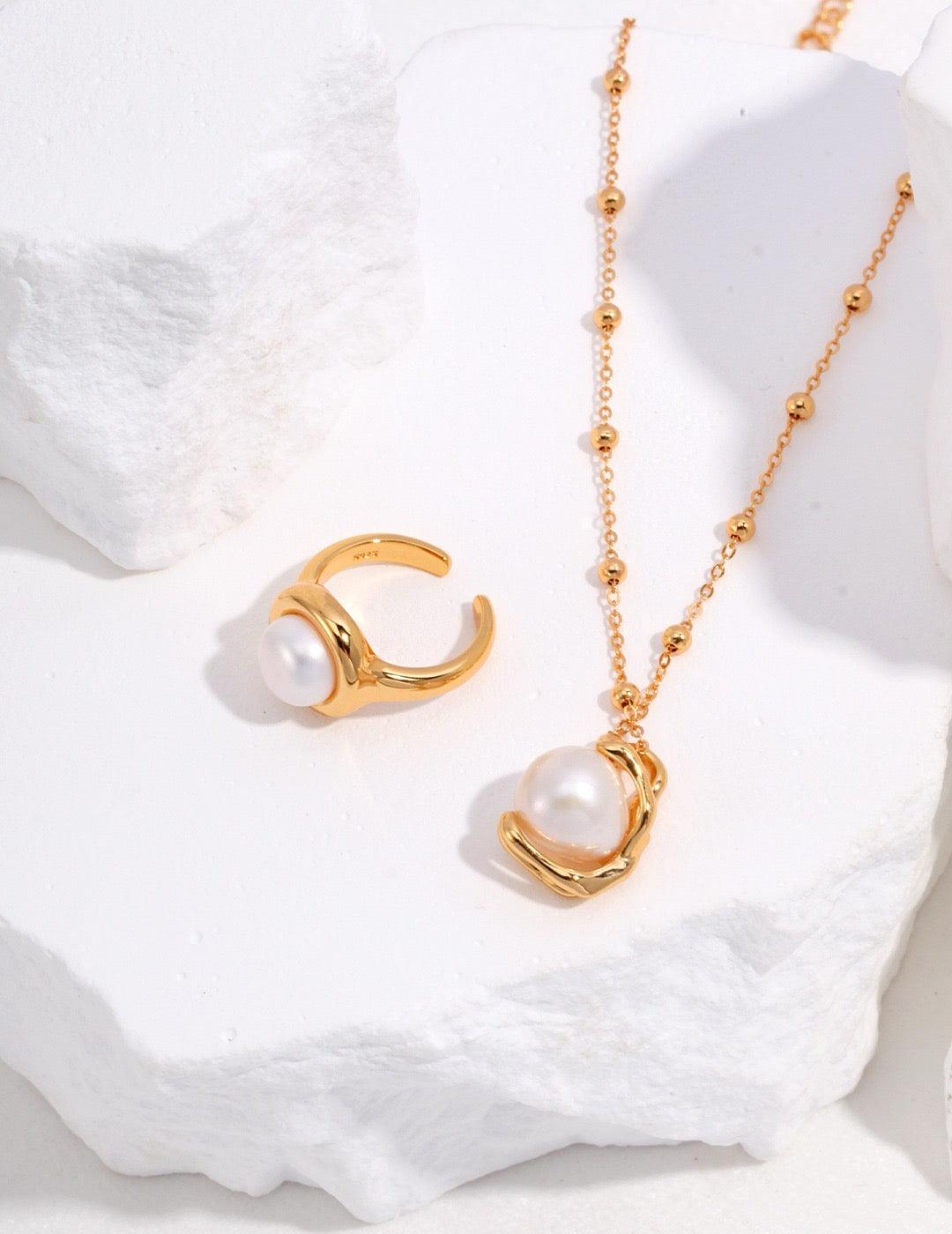 Elise Baroque Pearl Pendant Necklace and a gold pearl cuff ring displayed on the white rock.