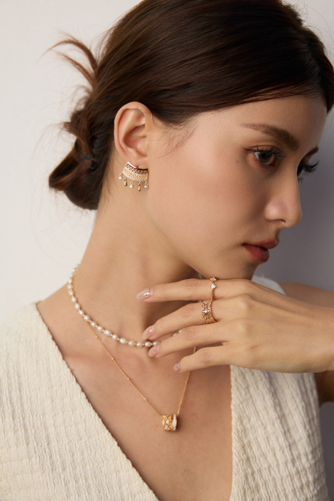 Woman wearing gold jewelry including a necklace, cascade earrings, and ring.