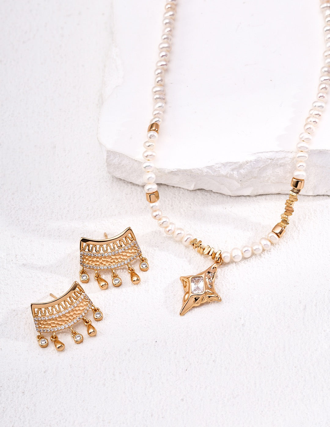 Gold earrings and necklace set on a white fabric background