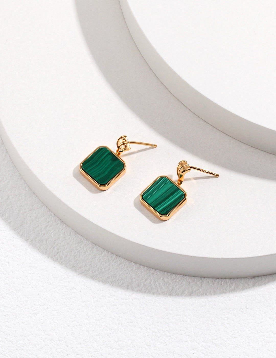 Gold earrings with green square malachite stones on a white background