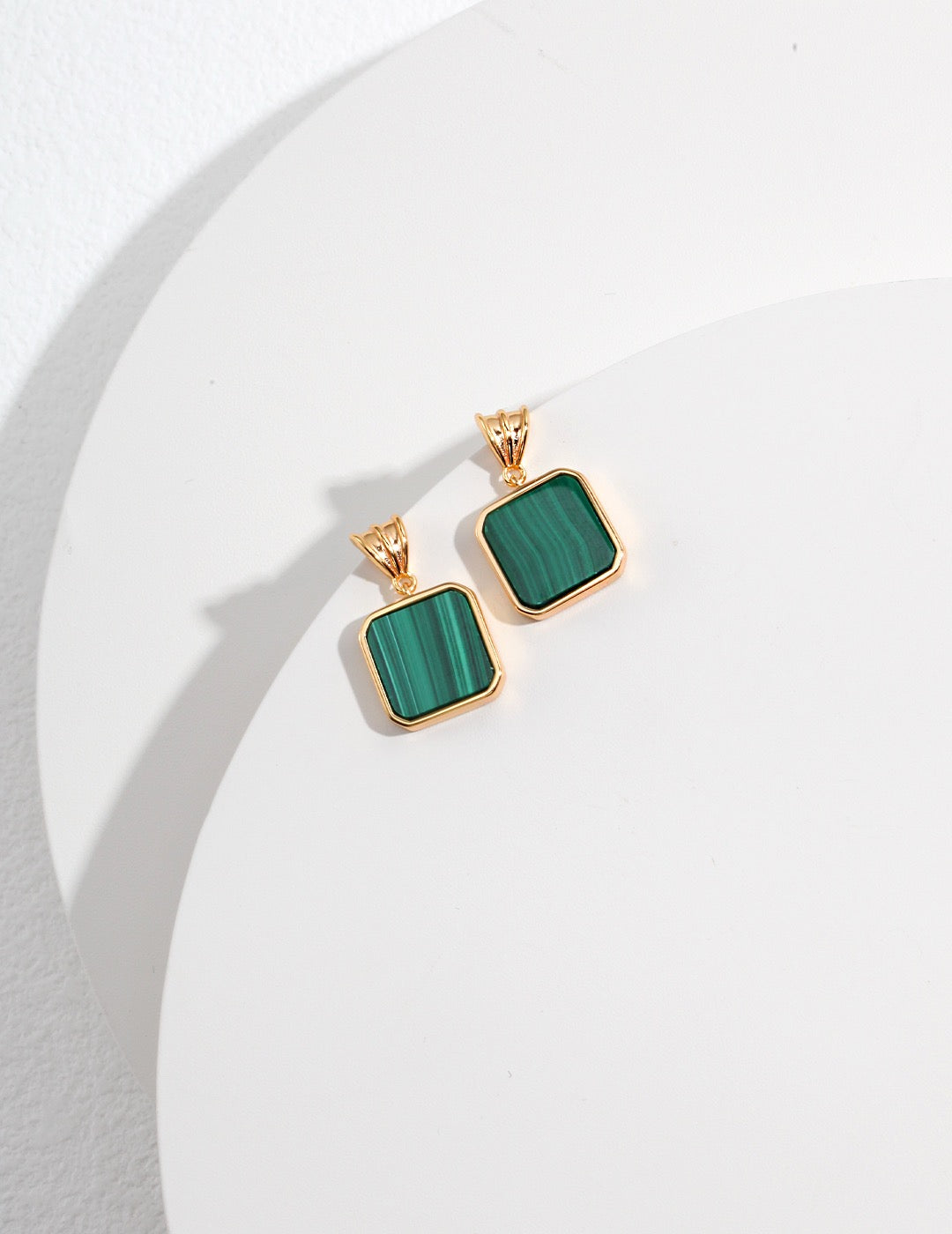 Gold earrings with green square malachite stones on a white background