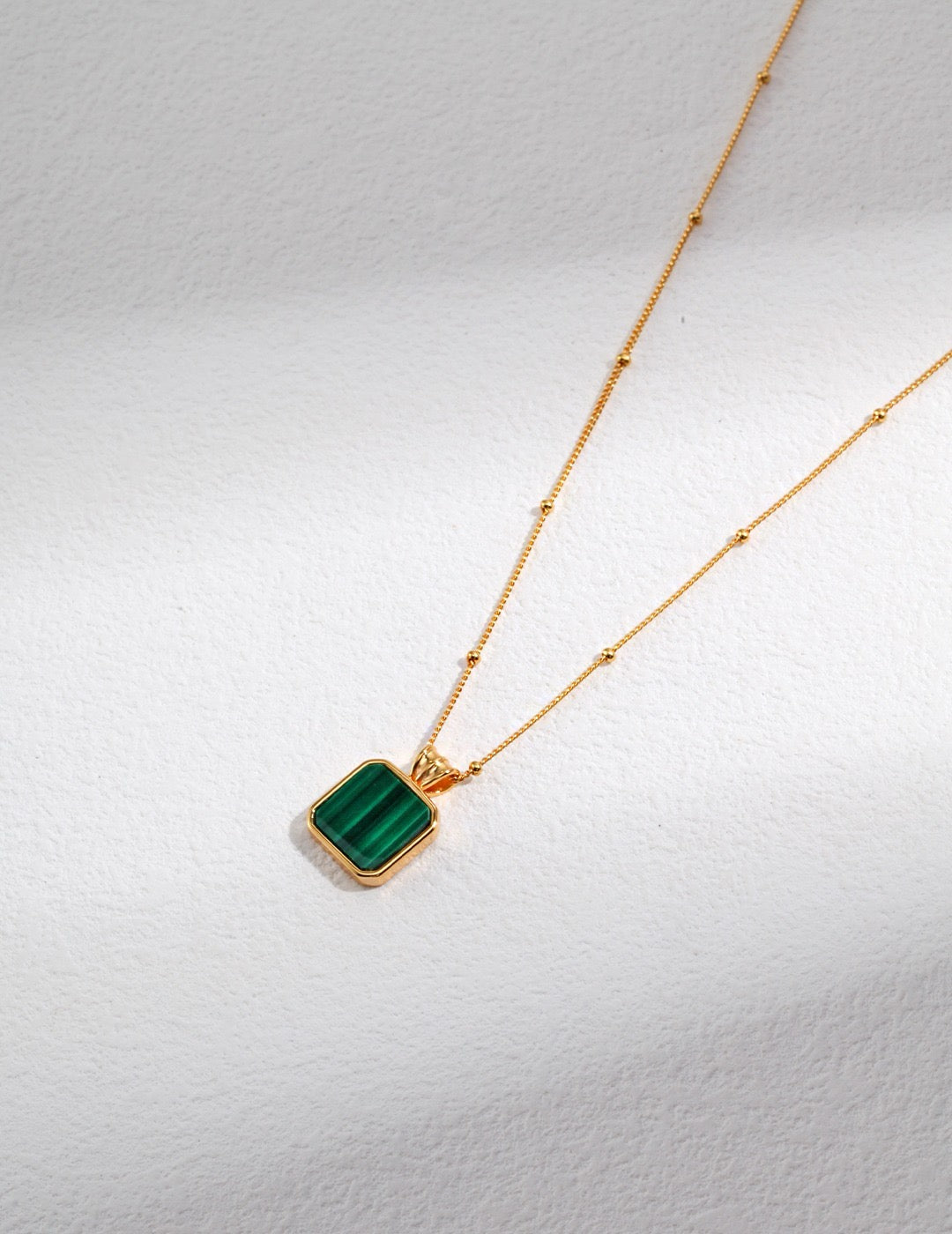 Gold necklace with a green malachite pendant on a light gray background