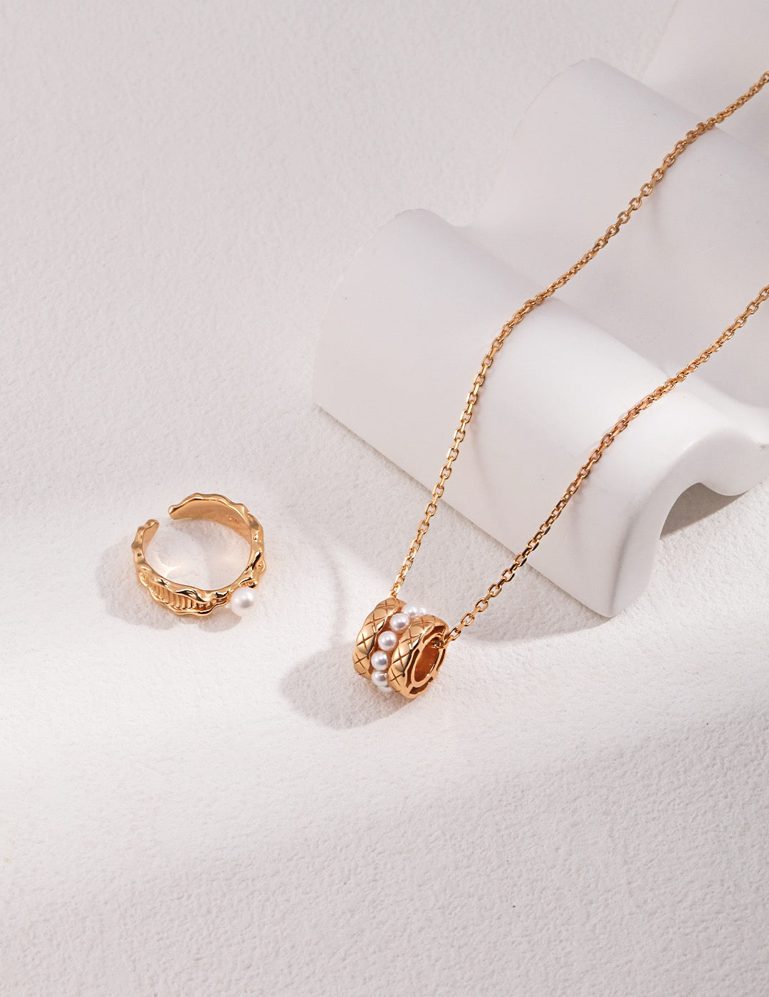 Gold necklace and ring on a light gray background