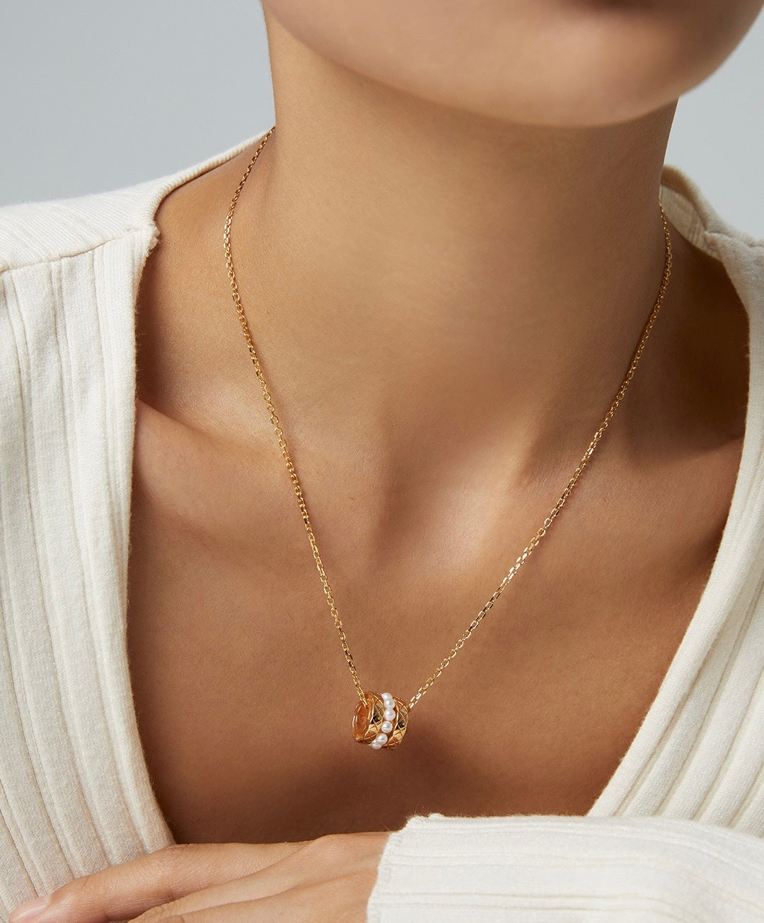 Gold necklace with a pendant on a person wearing a white sweater.