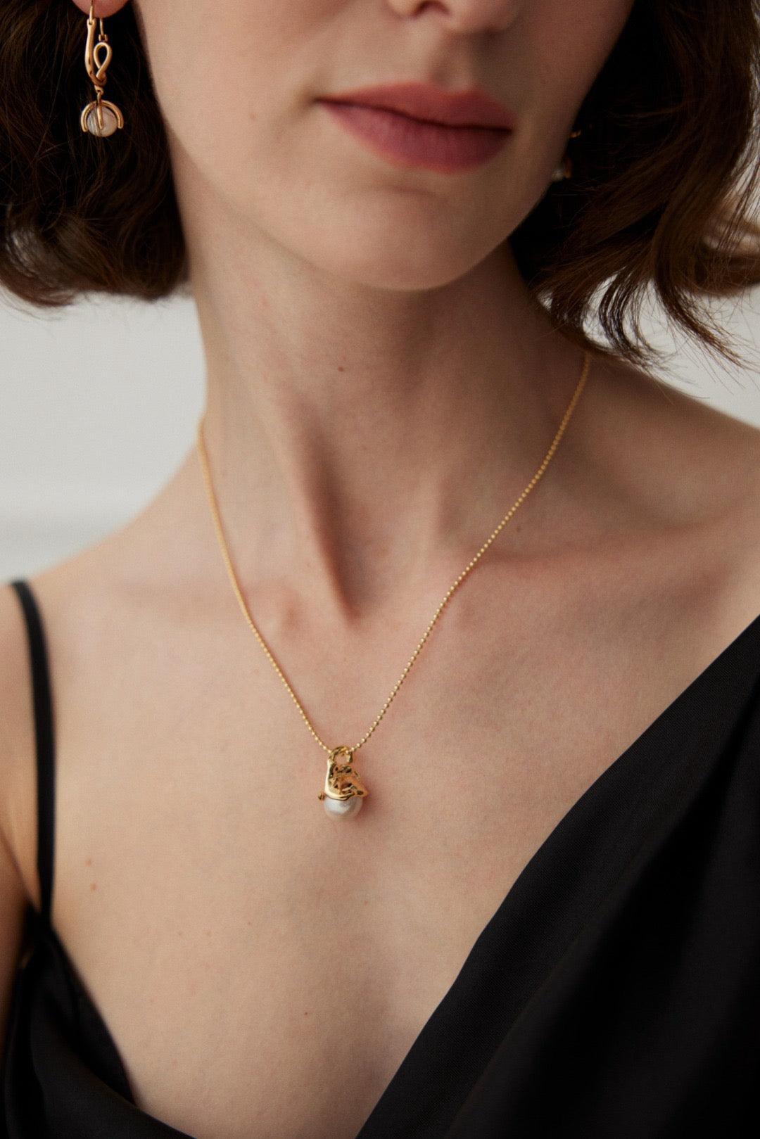 A women is wearing the gold pendant necklace with black V-neck dress.