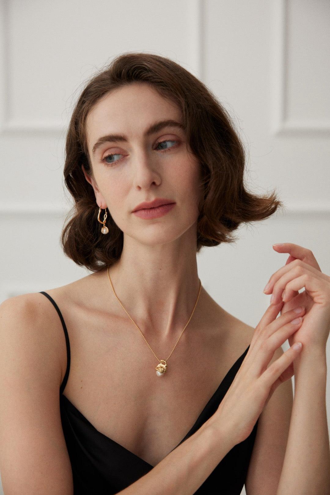 A wide shot of a women wear Flora Pearl Pendant Necklace with black V-neck dress against the white French Design interior background