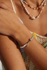 A person wearing a bracelet with a traditional Chinese character pendant, alongside other jewelry.
