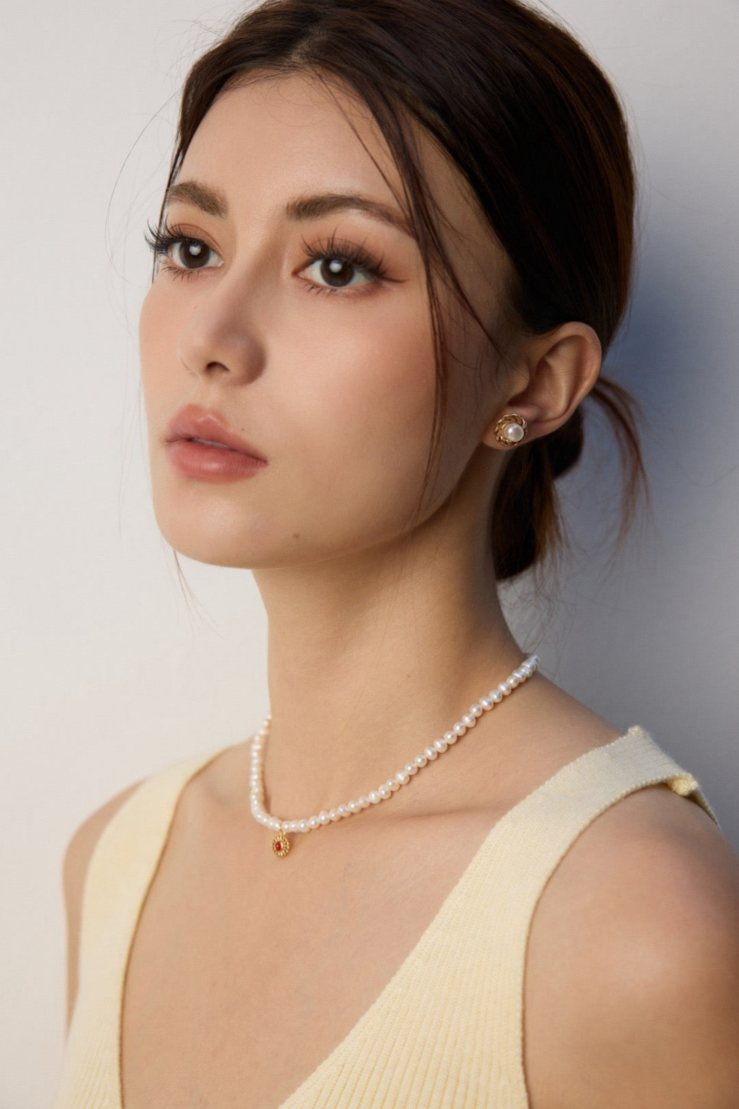 Woman wearing a pearl necklace and earrings against a plain background