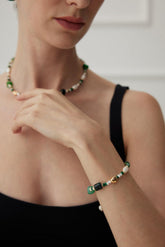 A person wearing a Glimmer Agate & Malachite Bracelet with a necklace in the background.