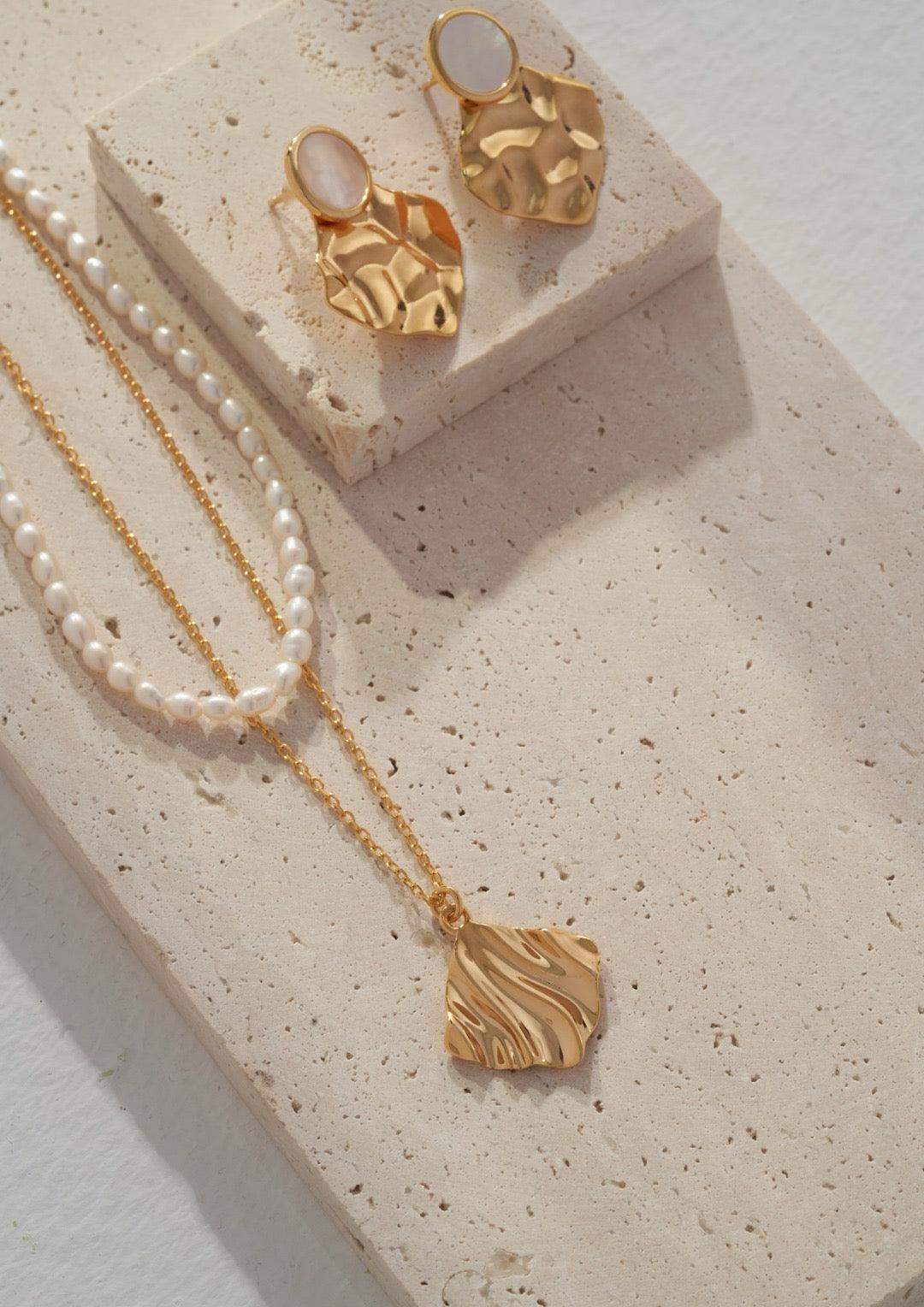 A front view of the pearl-layered pendant necklace and hoop earrings is displayed on the marble.