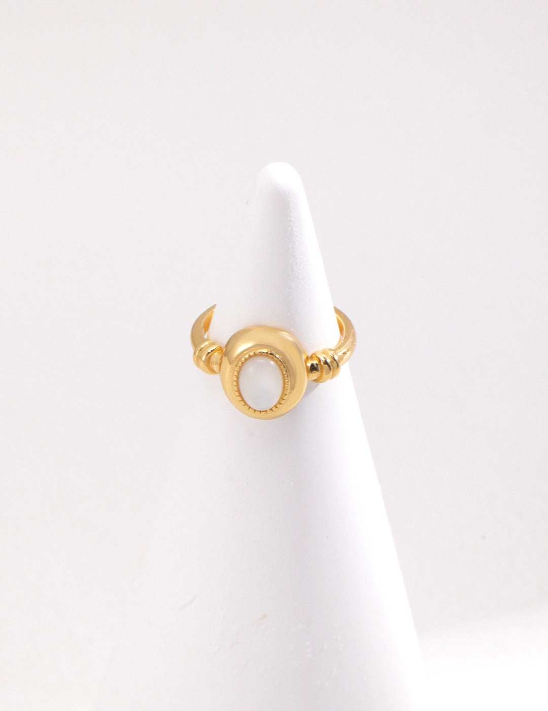 A gold-colored open band ring with a mother of pearl inlay displayed on the ring stand.