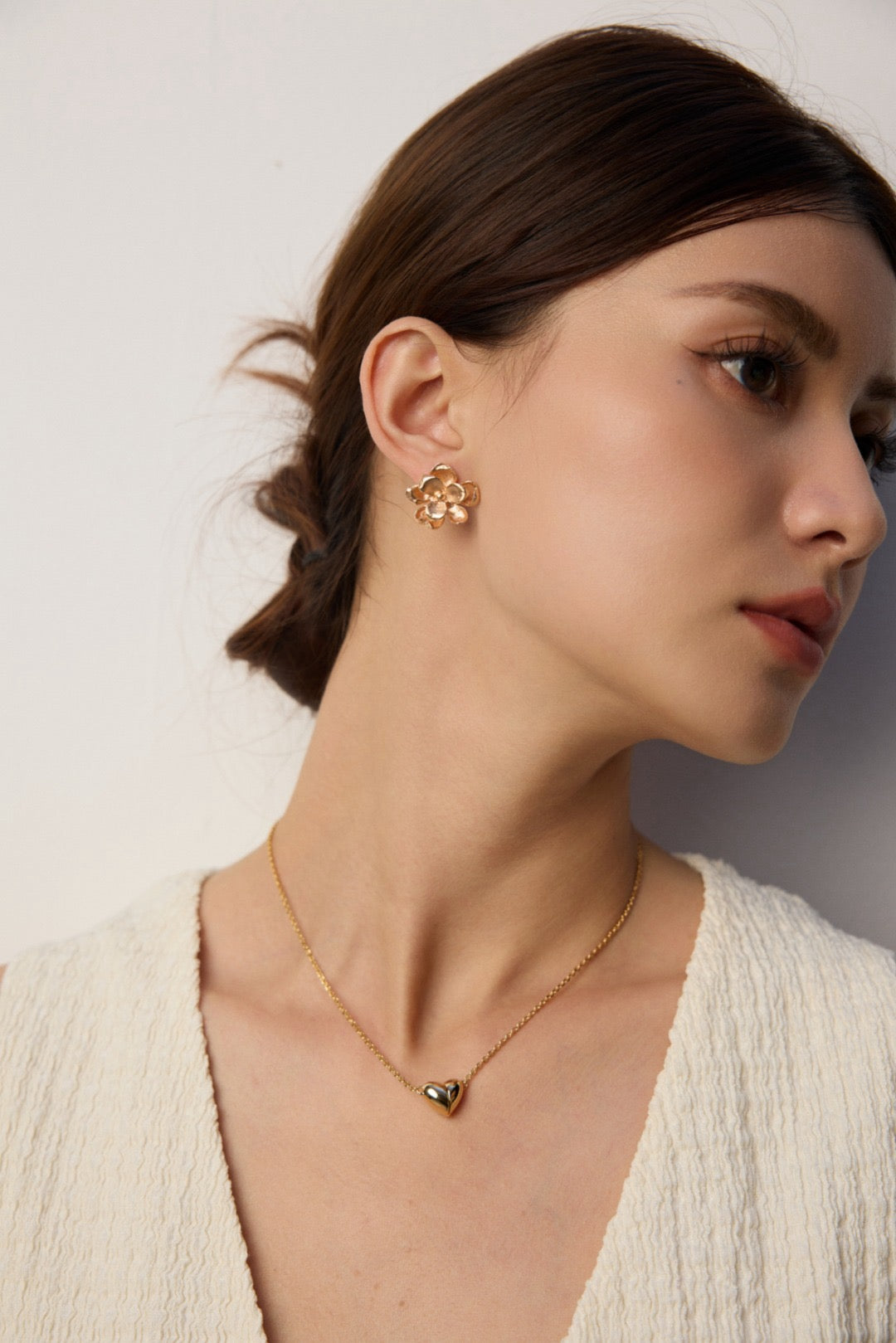Woman wearing a gold earring and necklace on a plain background