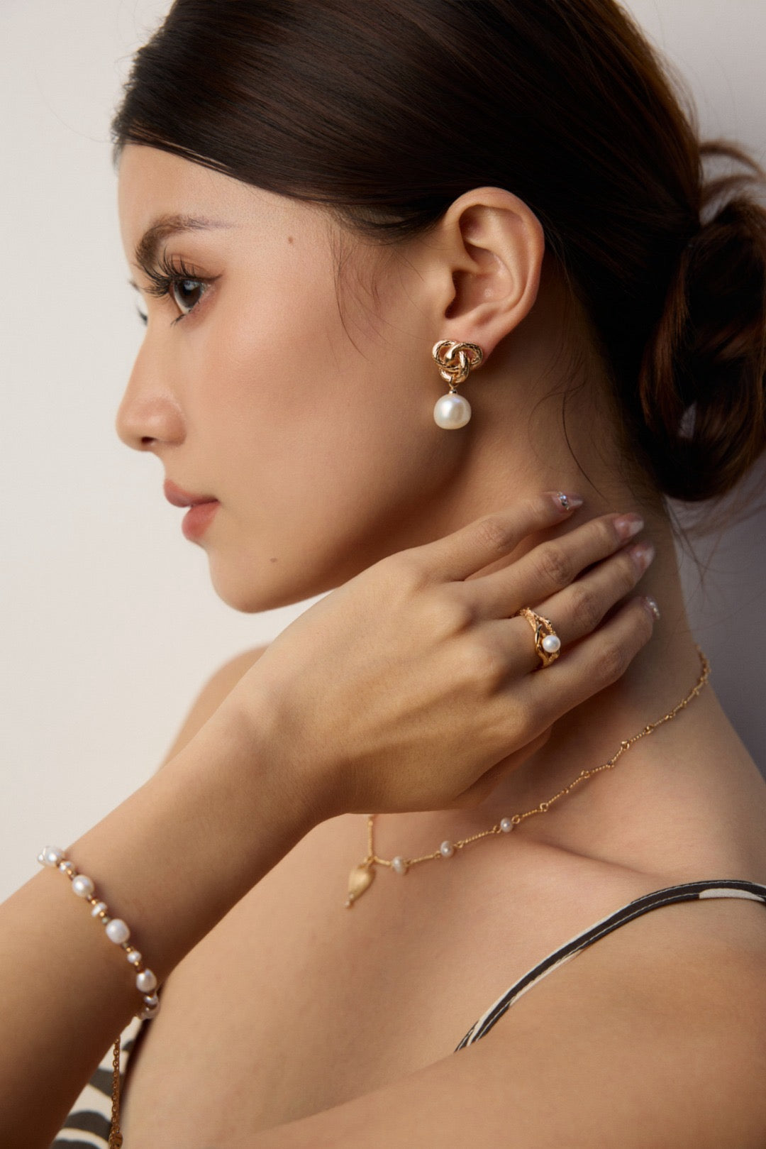 Woman wearing pearl jewelry including earrings, necklace, and bracelet against a neutral background