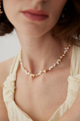 A close-up of a person wearing a white garment with a gold and pearl necklace.