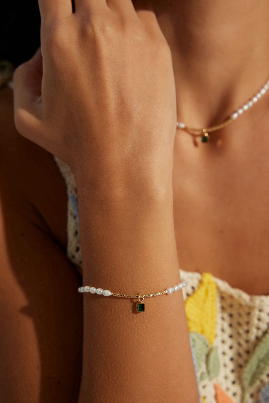 A person wearing a floral dress showcases a bracelet on their wrist. The bracelet appears to be composed of pearls with a zircon charm.