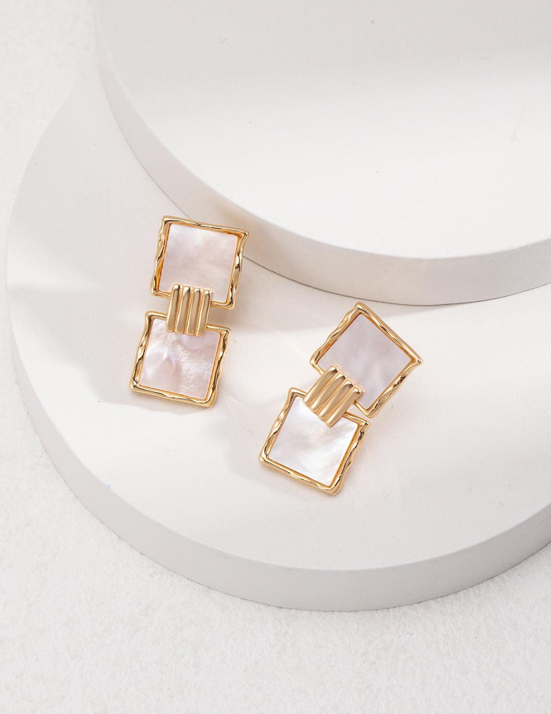 Karina Drop Earrings are displayed on two white circular stages.