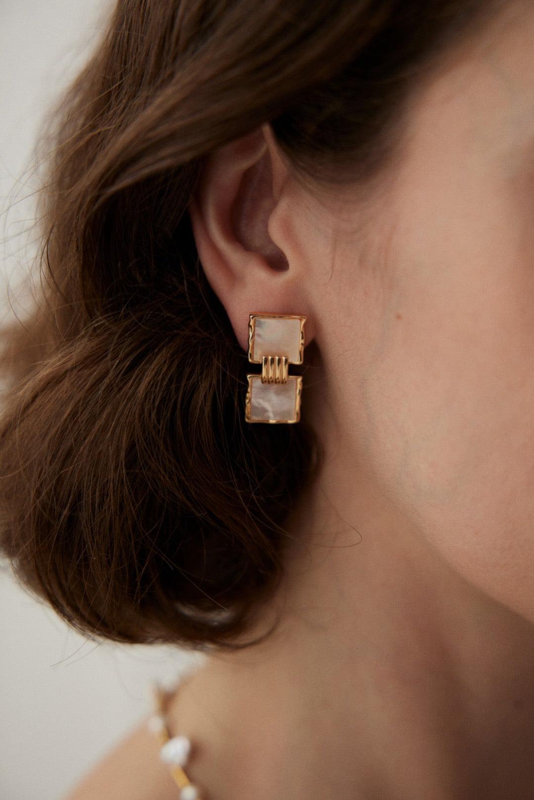 A close-up image of a person wearing square drop earrings with gold vermeil detailing.