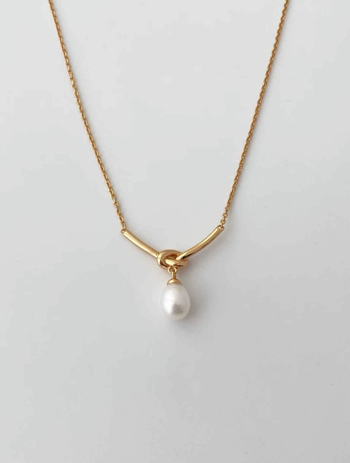 Gold necklace with a single pearl pendant on a light gray background