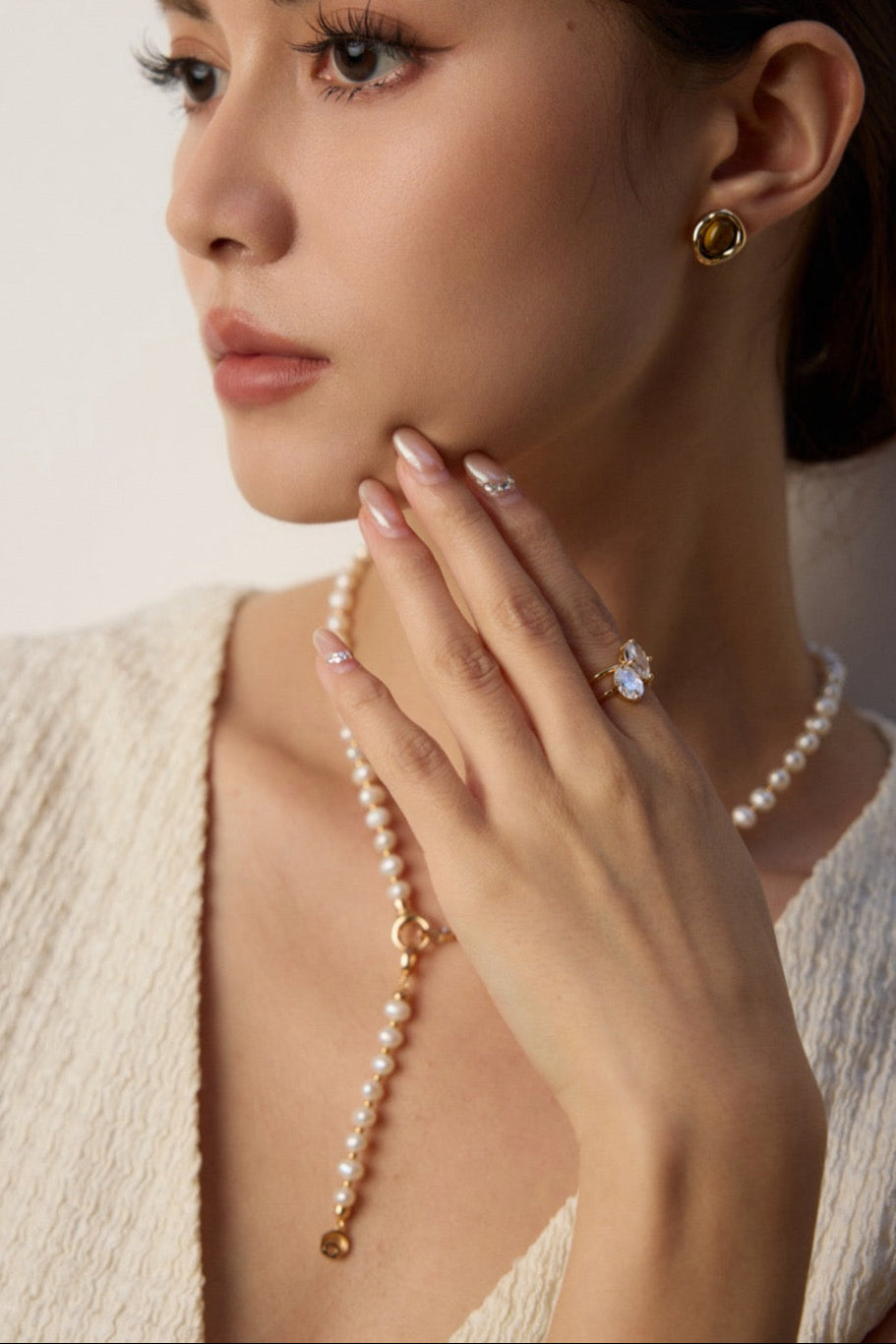 Woman wearing a pearl necklace and earrings against a neutral background