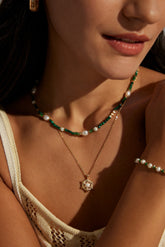 Close-up of a person wearing a delicate necklace with green beads and a gold pendant.