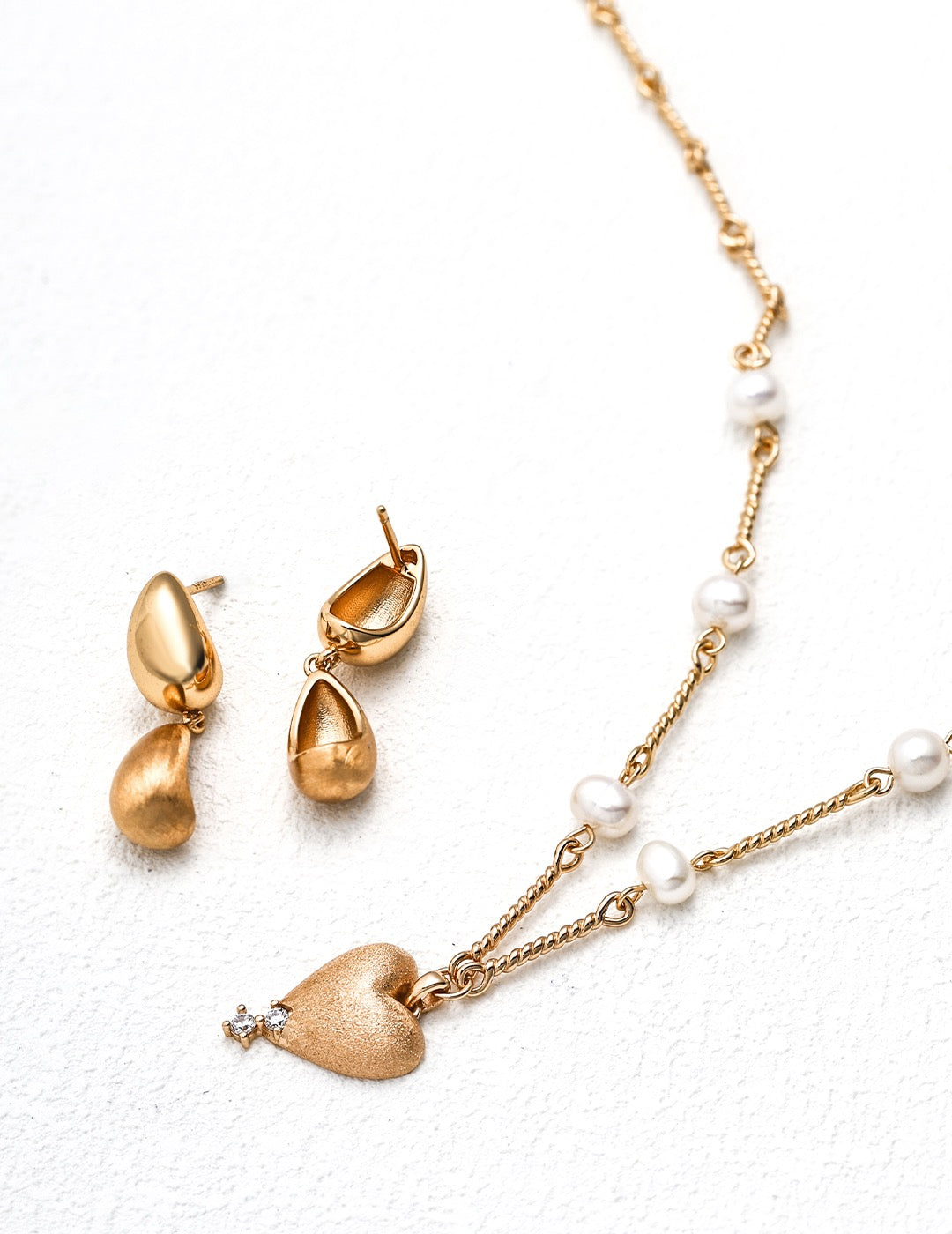 Gold earrings and necklace with heart pendant on a white background