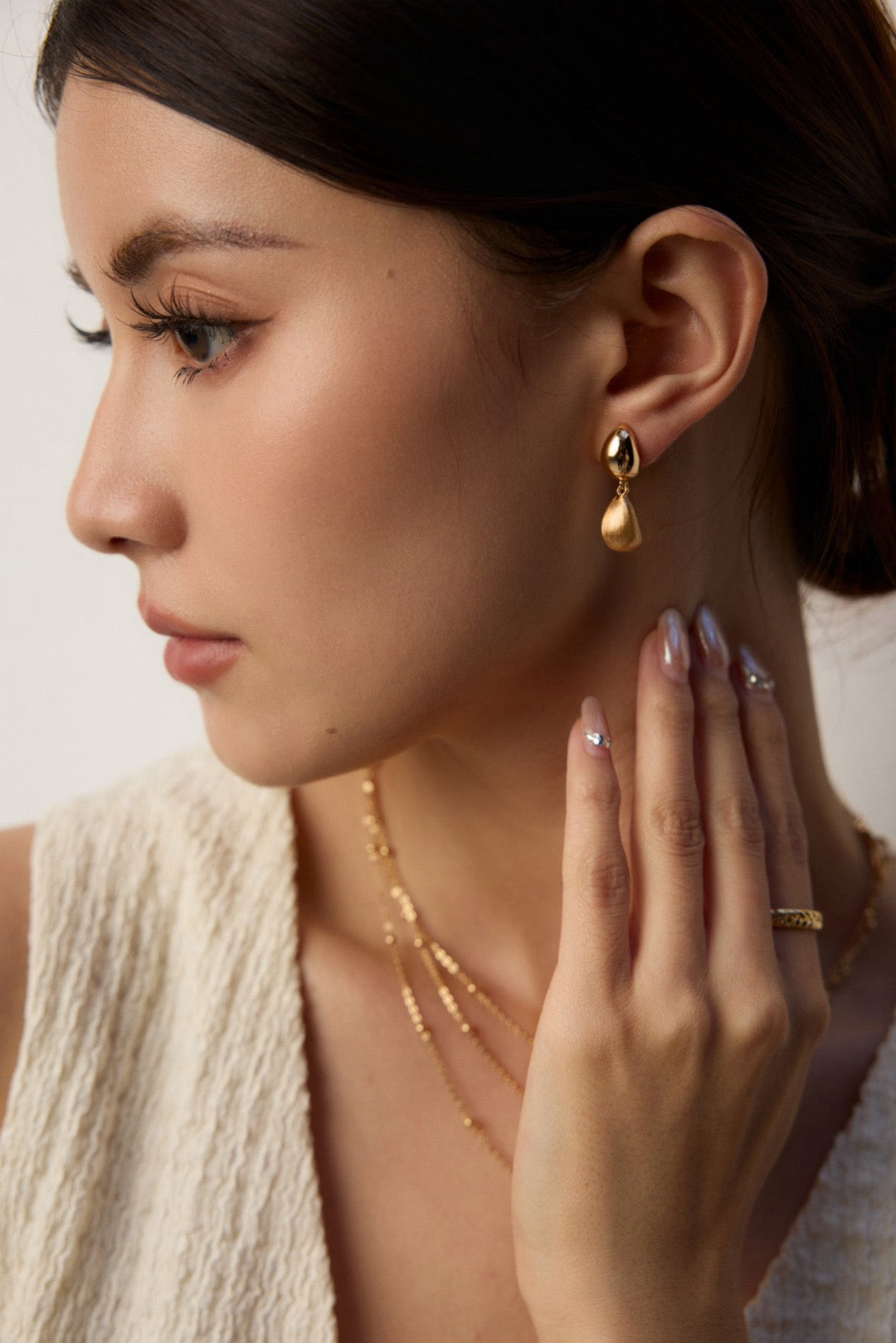 Woman wearing gold earrings and necklaces with a neutral background