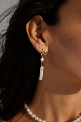 A close-up image of a woman's ear wearing a gold vermeil earring with a small pearl and a long baroque pearl drop.