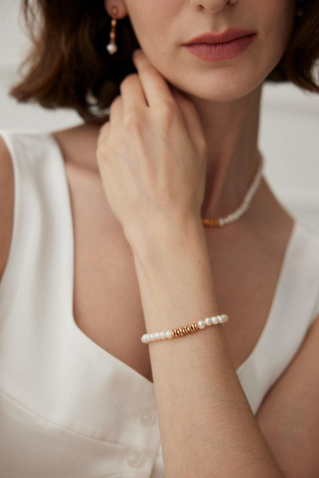 A woman wearing a white dress is showcasing a pearl bracelet with gold accents on her wrist.
