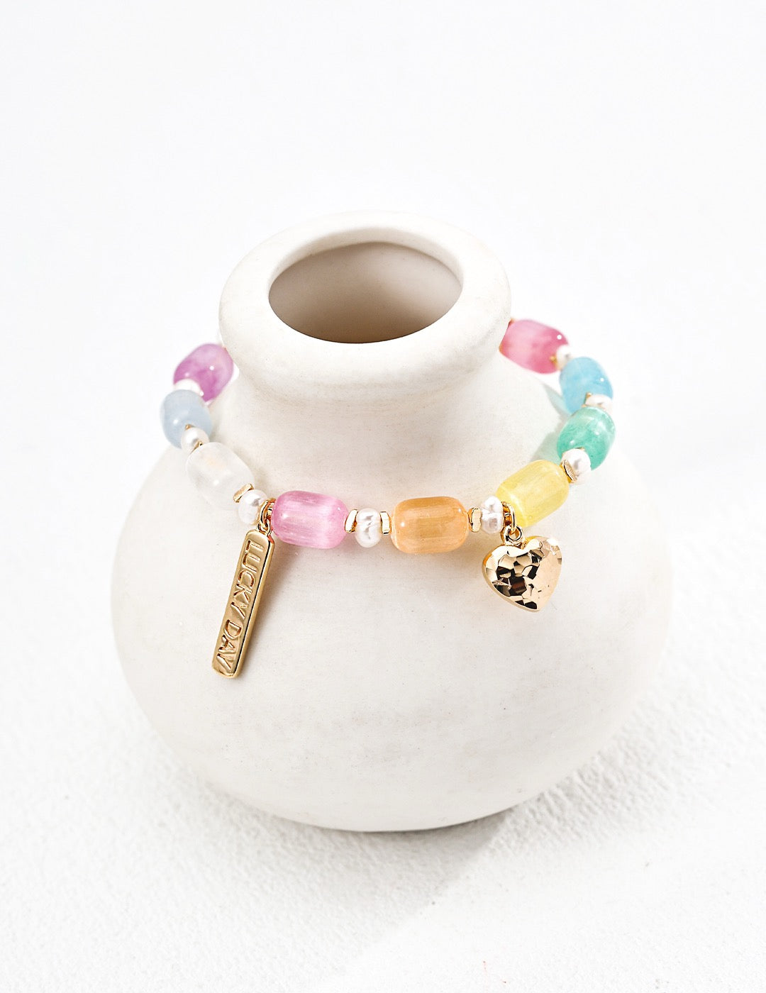 Colorful Lucky Day gemstone bracelet featuring pastel glass beads, freshwater pearls, and gold vermeil heart and charm details, styled on a neutral ceramic vase.