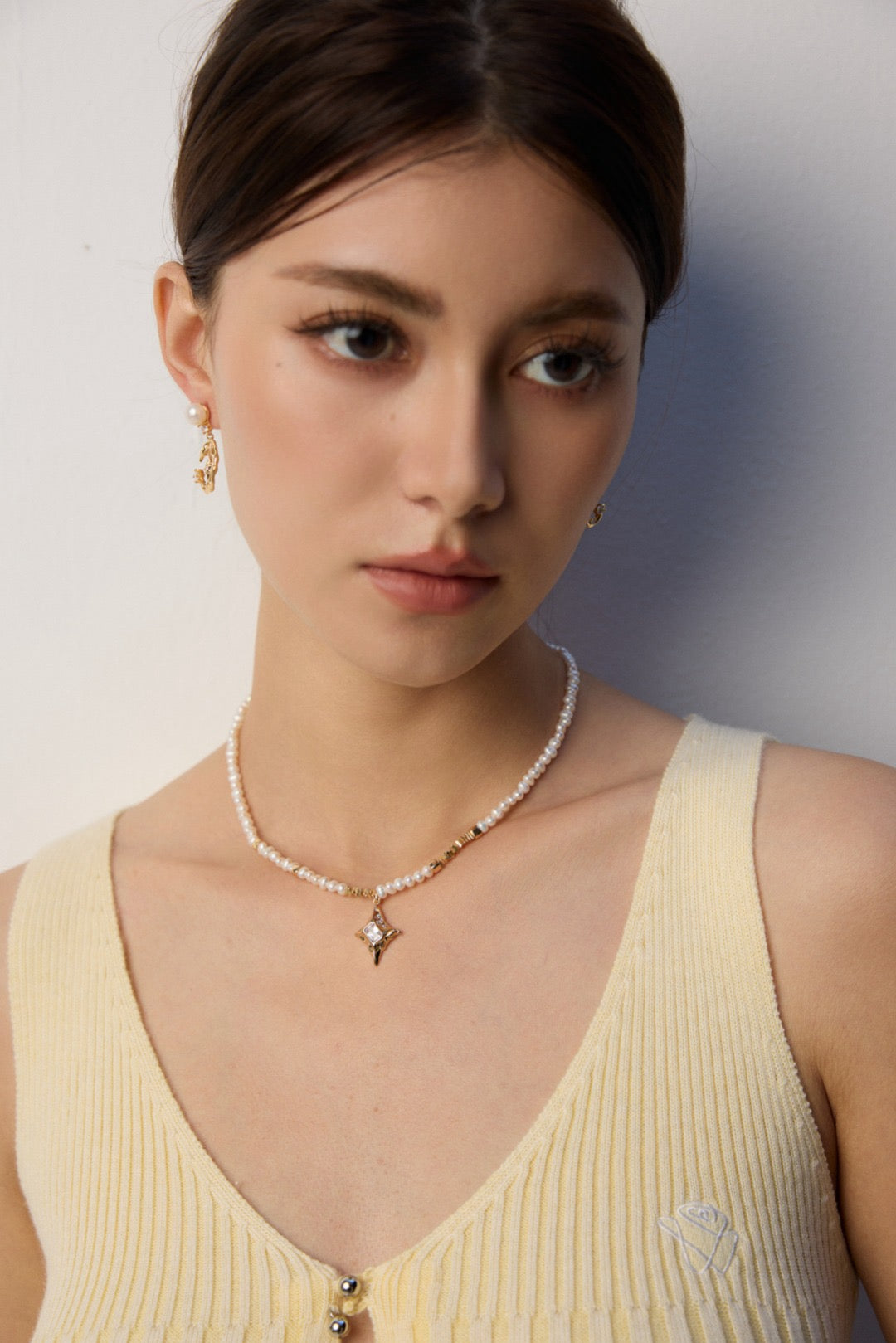 Woman wearing a pearl necklace and earrings against a neutral background