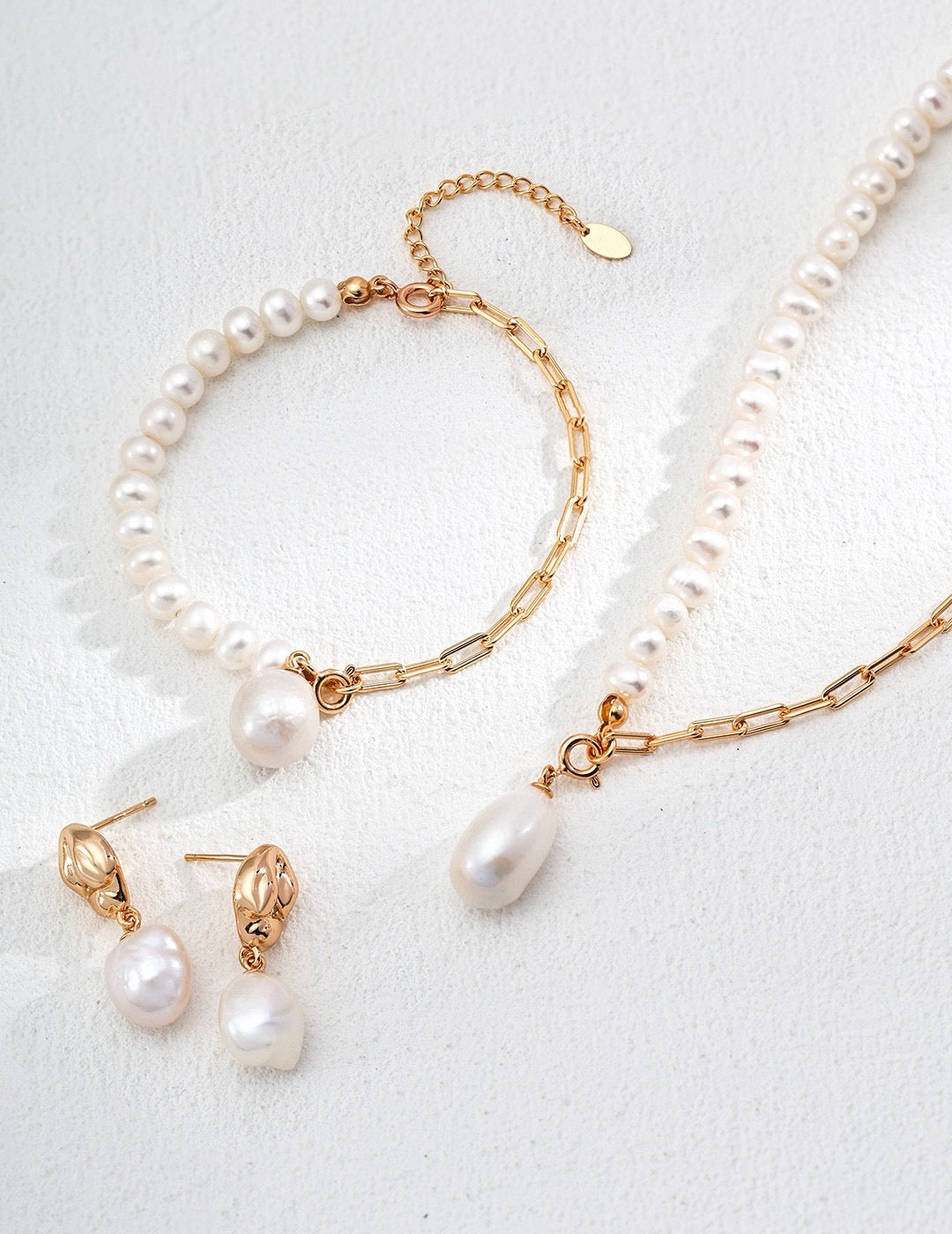 The Luna Dual-Chain Freshwater Pearl Bracelet and Necklace Set in gold, and the pearl drop earrings in gold are displayed on the white background. Focusing on the pearl charms