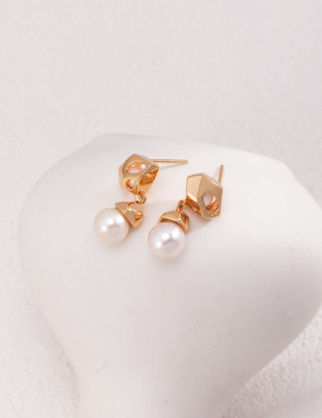 A close up of the Luna Pearl Drop Earrings in 18k Gold vermeil displayed on the white rock, showcasing the shine of the pearls.