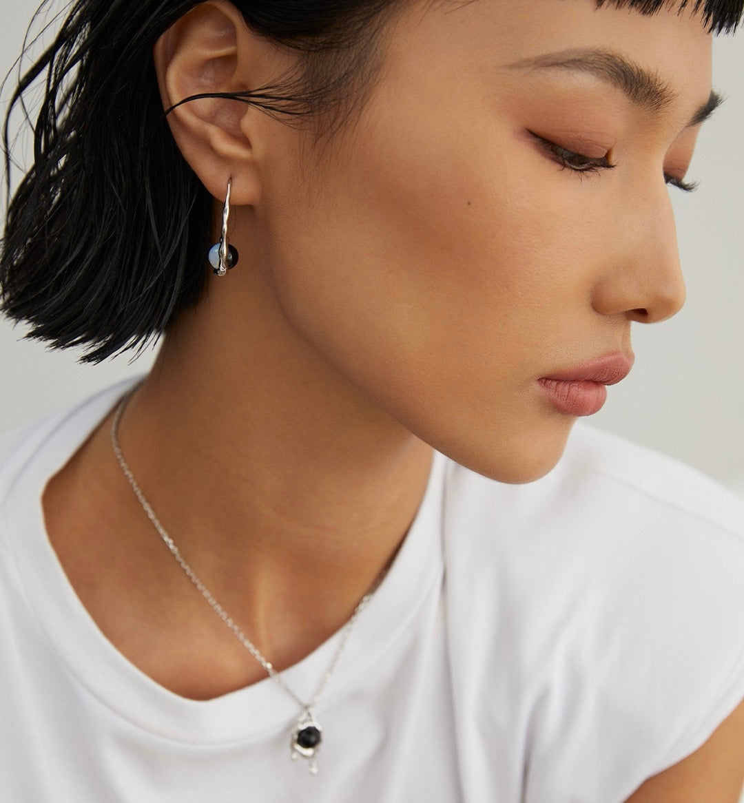 A lady is wearing the 18K gold vermeil earrings featuring a reversible design with opal on one side and black agate on the other, showcasing its minimalist design.